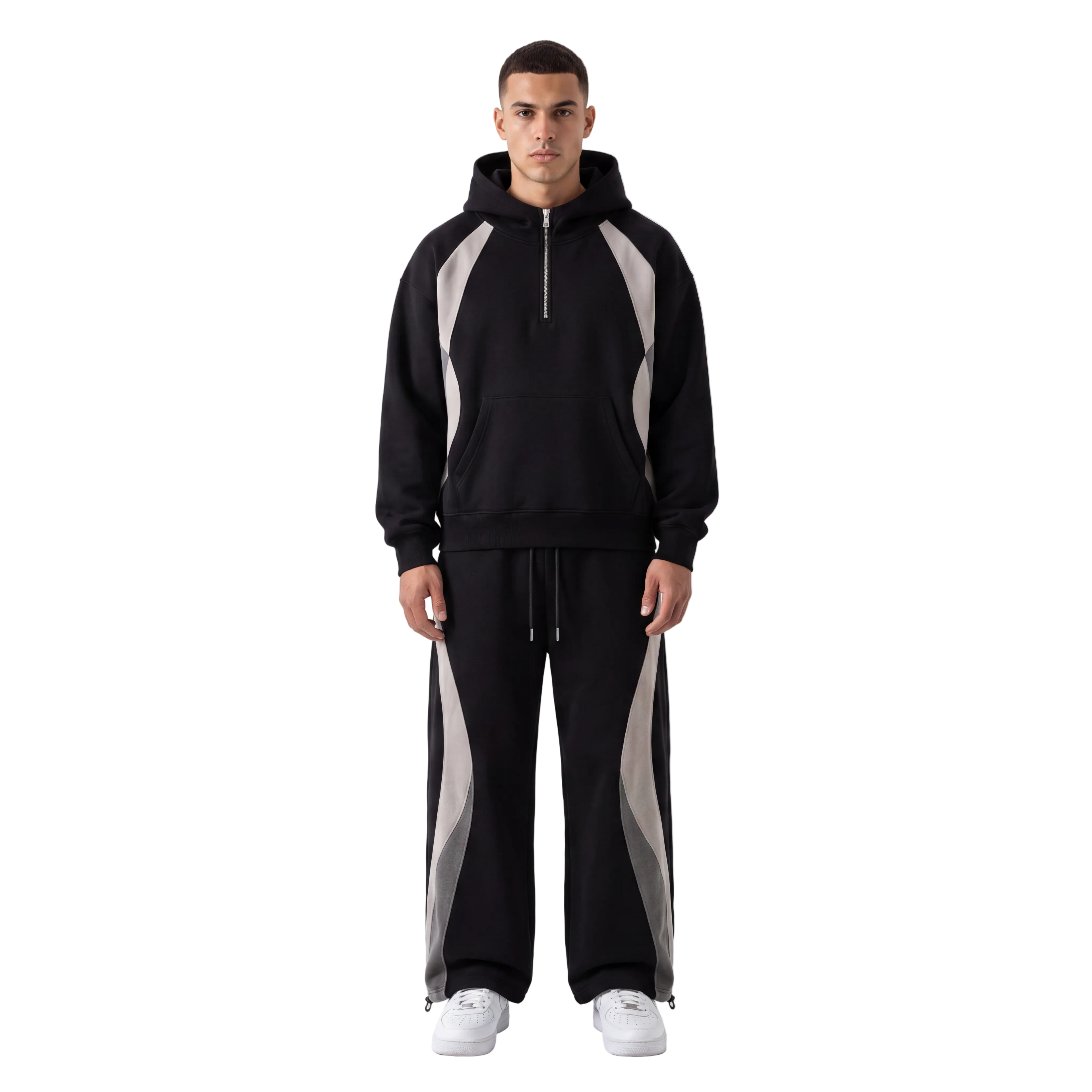 A man modeling a black half-zip hoodie and matching wide-leg sweatpants with light gray side panels, paired with white sneakers, against a plain white studio background.